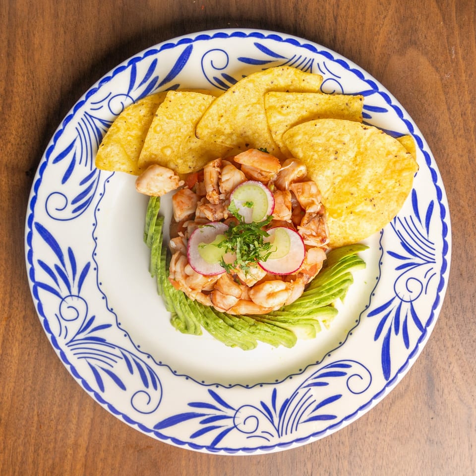 Encanto Alebrije's shrimp ceviche with avocado, radishes, and tortilla chips on a decorative plate.