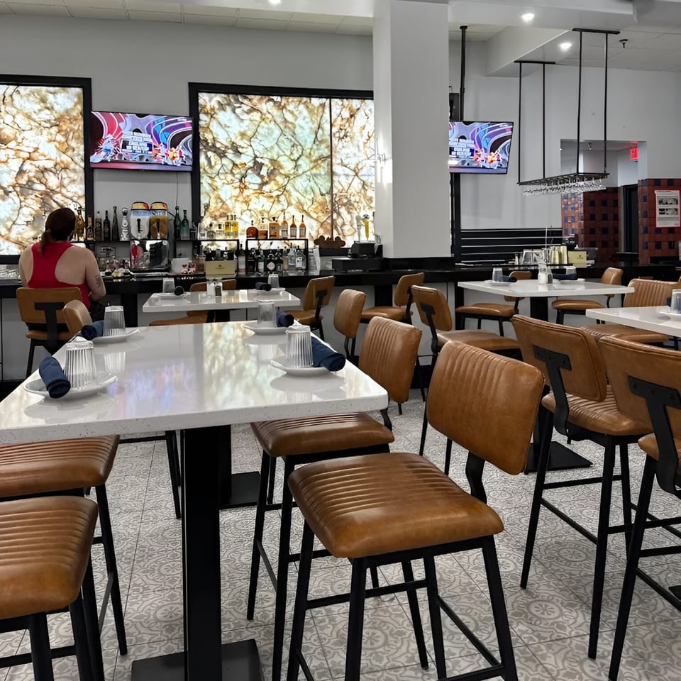 Interior of Encanto Alebrije, a Mexican restaurant, with high-top tables, brown leather chairs, and a bar.