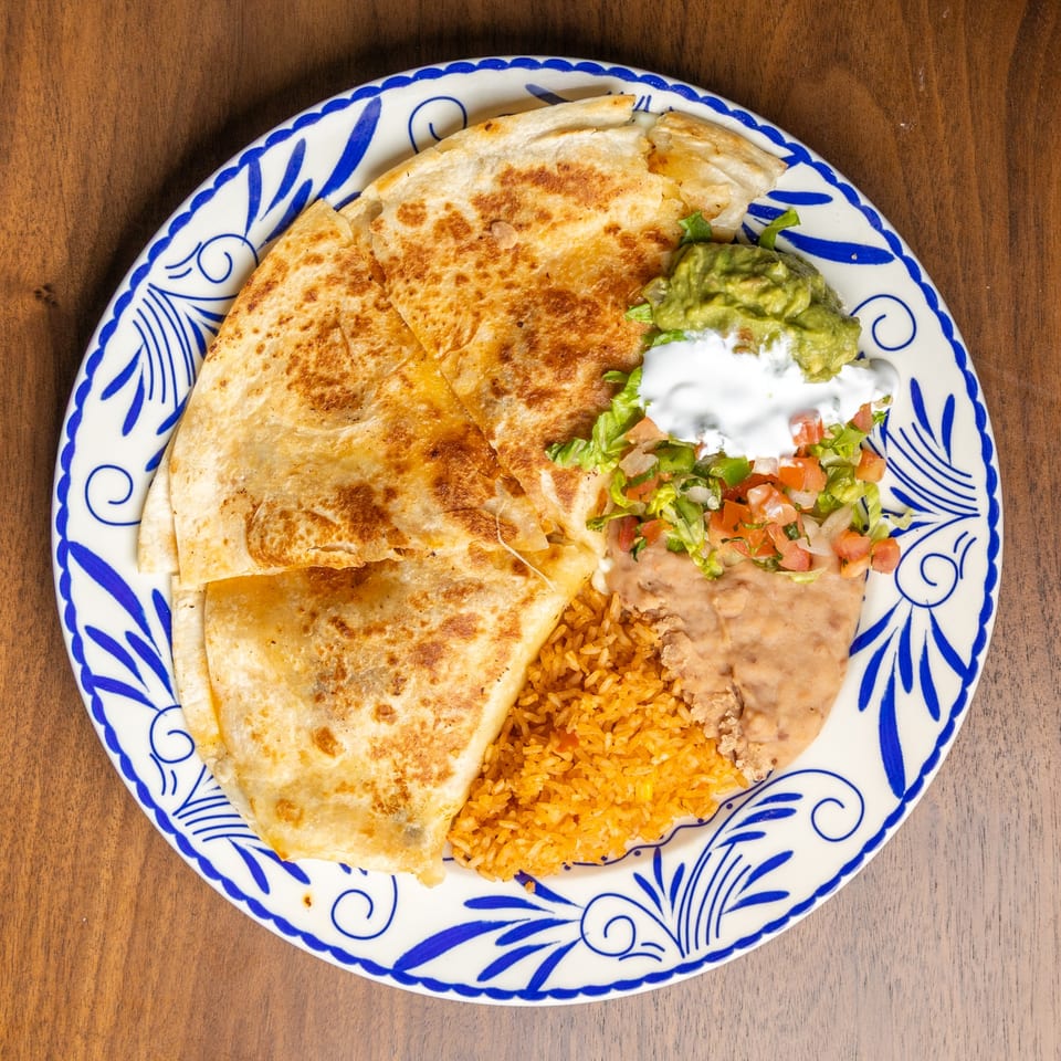 A quesadilla with rice, refried beans, guacamole, sour cream, and pico de gallo on a white and blue plate.