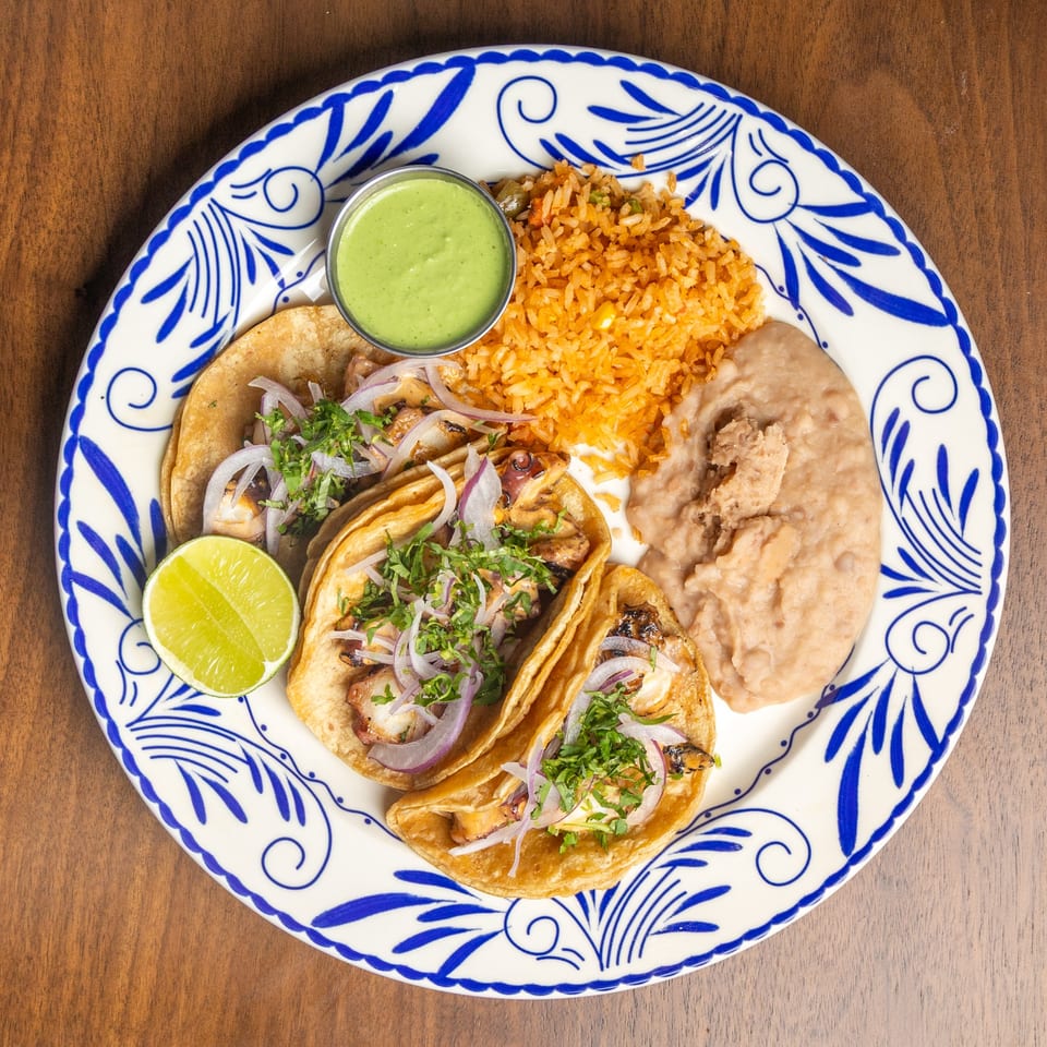 Three chicken tacos with onions and cilantro, served with rice, refried beans, and green salsa.
